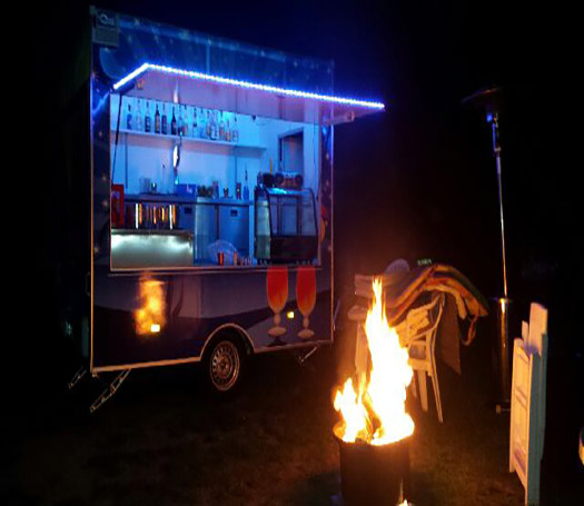 Eine Feuertonne vor dem Cocktailwagen bei Nacht